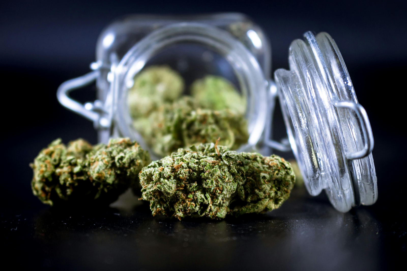 A premium glass jar filled with high-quality green cannabis buds on a clean white background